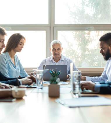 Colleagues Working During Corporate Meeting Sitting At Desk In Office