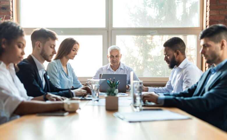 Colleagues Working During Corporate Meeting Sitting At Desk In Office